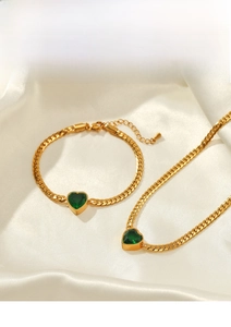Detail of gold curb chain necklace and bracelet set with green heart-shaped gemstones