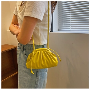 Close-up of a bright yellow pleated dumpling bag worn crossbody with blue jeans