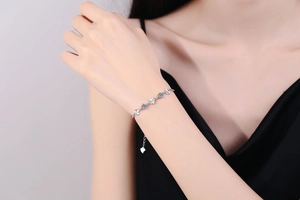 Detail view of S925 silver four-leaf clover bracelet with blue moissanite on a model's wrist