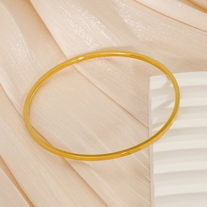 Detailed view of a slim gold minimalist stainless steel bangle on beige silk fabric