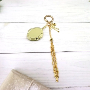 Close-up of golden mesh charm keychain with ribbon, oval locket and metal tassels