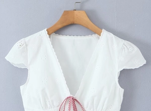 Close-up of white V-neck top with delicate eyelet embroidery and a red checkered bow