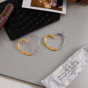 Detail of heart-shaped 18K gold and silver steel earrings with hammered texture finish