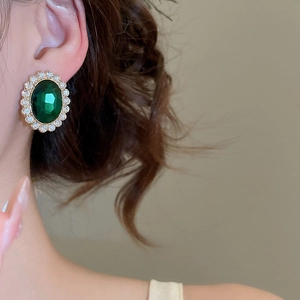 Detailed close-up of a vintage oval emerald stud earring with a diamond halo design