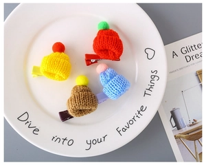 Detail of four handmade knitted mini hat hair clips with colorful pom poms in a white tray
