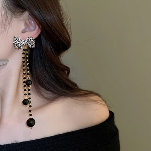 Detail of leopard bow earrings with long black tassels worn by a model on green background