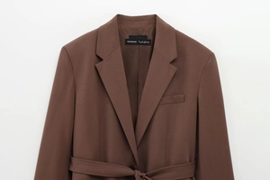 Detail of dark brown blazer featuring peak lapels, chest pocket, and adjustable waist belt