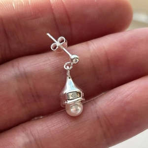 Detailed macro view of S925 silver pearl drop earring held between fingers