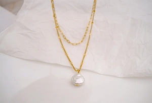 Detail of layered gold paperclip chain and baroque pearl pendant on textured surface