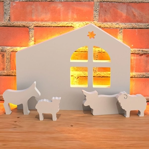 Detalle de siluetas de belén de madera blanca con retroiluminación cálida y suave