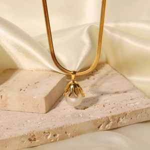 Detail of white pearl pendant on golden snake chain over beige marble and silk background
