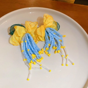 Detail view of handmade yellow floral fabric and blue beaded tassel earrings on white plate