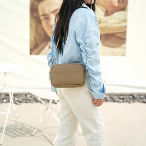 Rear view of model wearing a brown litchi grain PU leather crossbody bag over a blue shirt