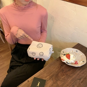 Detail of corduroy makeup bag with embroidered smiley faces held by a model