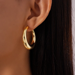 Close-up of model wearing gold chunky teardrop hoop earring with a polished mirror finish