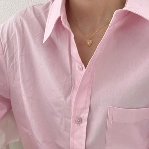 Close-up of a delicate gold heart necklace with a white stone on a pink shirt