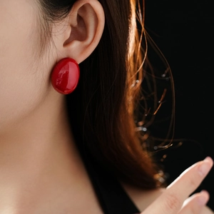 Detailed close-up of glossy red oval earrings on model with high-shine enamel finish