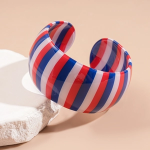 Macro detail of acrylic striped cuff bracelet on a minimalist white stone pedestal