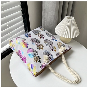 White linen tote bag with colorful pineapple print and thick rope handles on a white table
