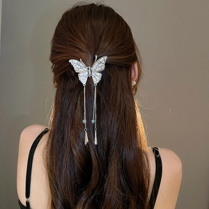 Détail de la pince à cheveux papillon argentée avec strass et pompons sur un modèle