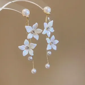 Elegant gold tassel earrings with white flowers and pearls on a warm gradient background