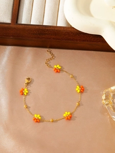 Detail of yellow and orange floral beaded bracelet with adjustable gold chain on silk