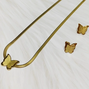 Detail of gold butterfly jewelry set with snake chain necklace and stud earrings on plush