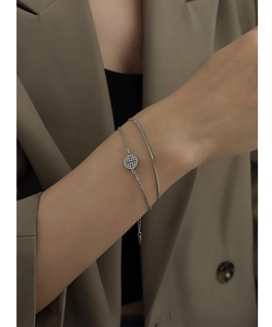 Close-up of double-layered silver snake chain bracelet with round hollow pendant charm