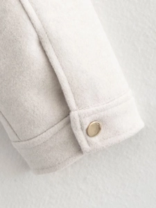 Close-up of off-white thick wool jacket sleeve with elegant gold metal button detail
