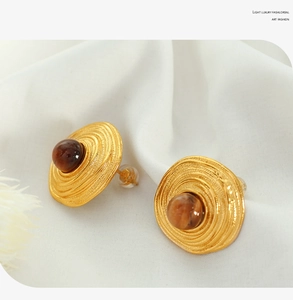 Detailed close-up of gold-tone earrings with tiger eye stones on white silk fabric
