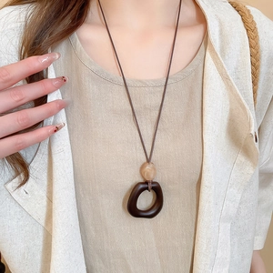 Detailed close-up of a vintage resin and wood oval pendant necklace on a linen garment