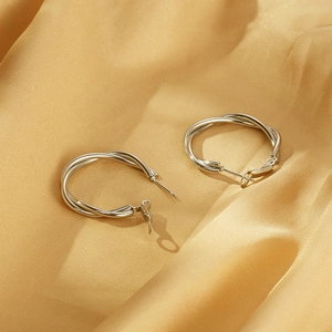 Detailed close-up of silver twisted hoop earrings on luxurious gold silk fabric background