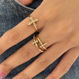 Détail de bagues croix plaquées or 18K avec strass brillants sur fond en denim
