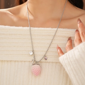 Detail of pink strawberry pendant necklace with heart and star charms on white knitwear