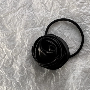 Close-up of a premium black satin rose hair tie on a white textured background