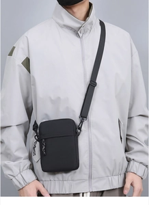 Close-up of a black nylon crossbody bag worn over a grey jacket with adjustable strap