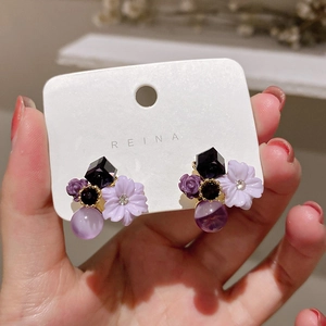 Detail showing vintage purple flower earrings with black gems and beads held by hand