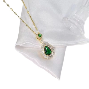 Elegant gold necklace featuring a green pear-shaped drop pendant on white satin