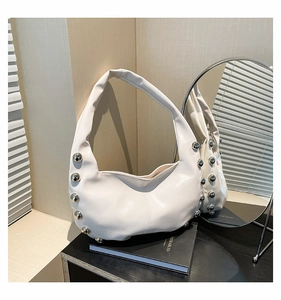 Close-up of white glossy hobo bag with silver metallic studs on a black book