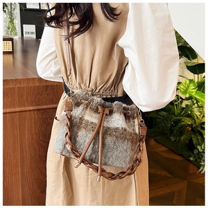 Detail of wool plaid bucket bag featuring a drawstring closure and brown PU leather strap