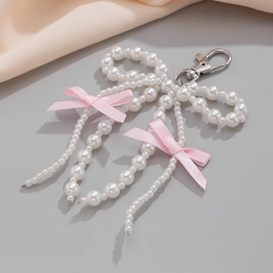 Detail of handmade pearl bow keychain with pink ribbons and silver lobster clasp on satin