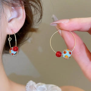 Detail of gold hoop earrings with red polka dot glass beads and small red spherical accents