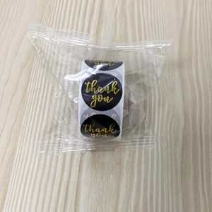 Macro shot of 1-inch black and gold foil Thank You adhesive stickers roll in poly bag