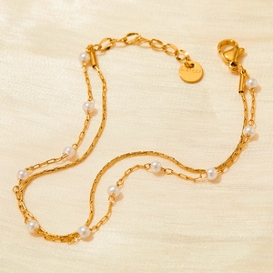 Double-layered gold stainless steel bracelet with small white pearls on beige fabric