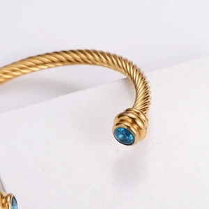 Gros plan d'un bracelet torsadé doré orné de deux pierres précieuses bleues facettées