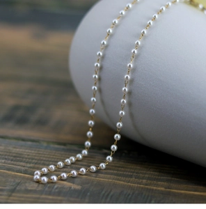 Close-up of fine cream pearl necklace with light gold chain on a wooden surface