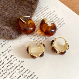 Macro shot of amber resin C-shape earrings on retro book and brown knit fabric background