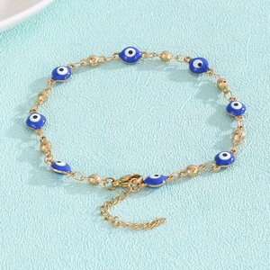 Detail of gold evil eye bracelet with blue beads on textured blue background
