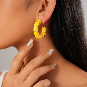 Detail view of a yellow and silver geometric C-shape enamel earring on a model ear