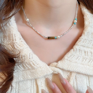 Detail of beaded necklace with tiger eye stone and pearls on beige knit sweater